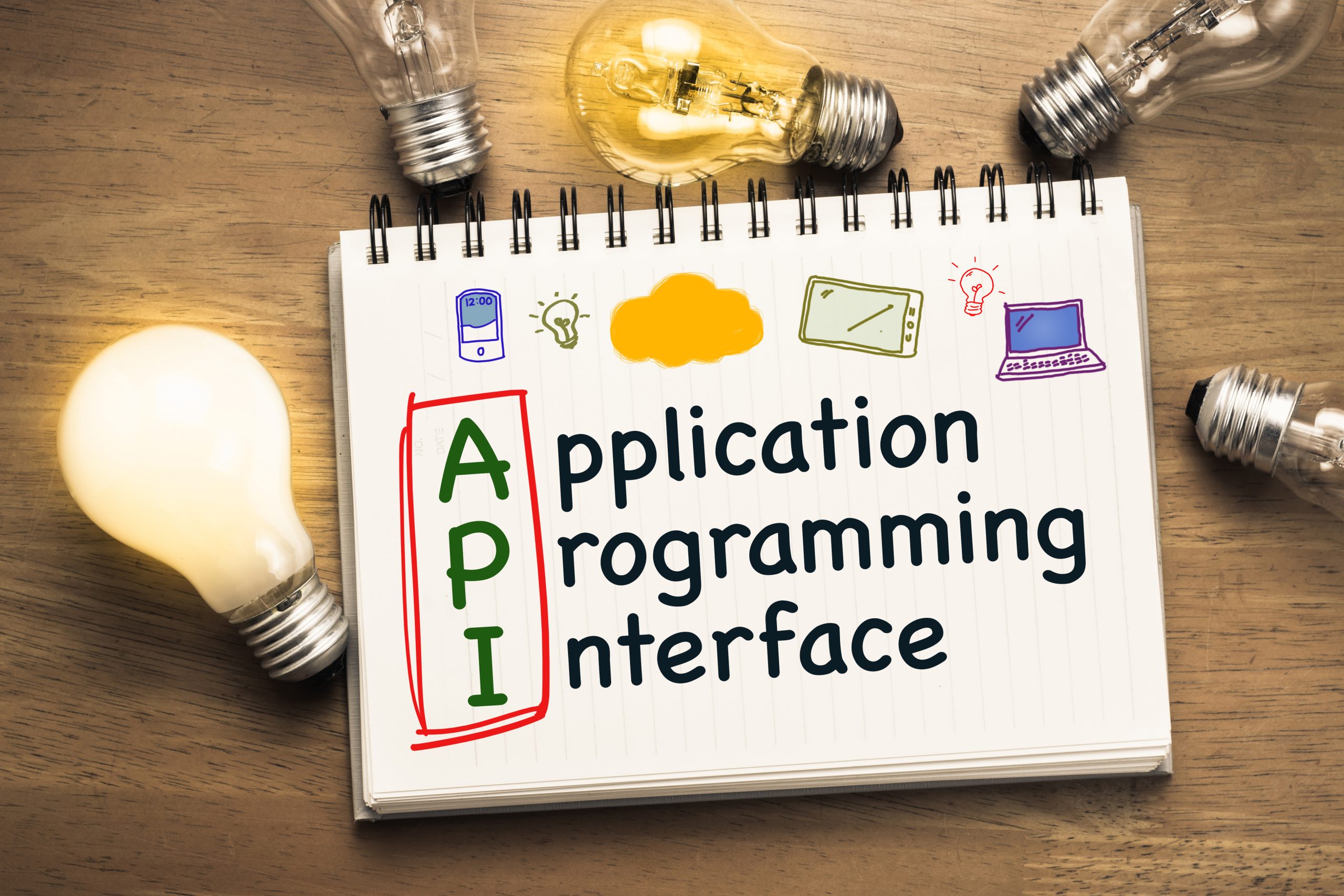 API (Application Programming Interface) text with drawing of device on notebook and glowing light bulbs