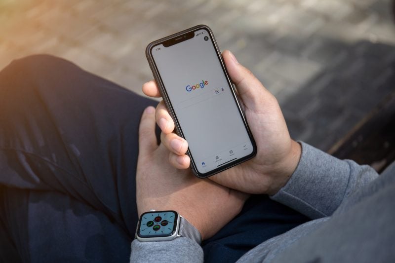Man hand with Apple Watch holding iPhone 11 with Google
